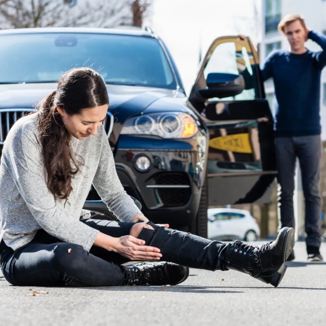 a girl in black jeans and shoes holding her injured knee as a concerned driver who hit her looks her way - pedestrian injury attorneys in columbus