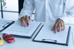 person reviewing car insurance documents on desk with toy car models