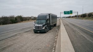 semi-truck stopped on highway shoulder near concrete median barrier